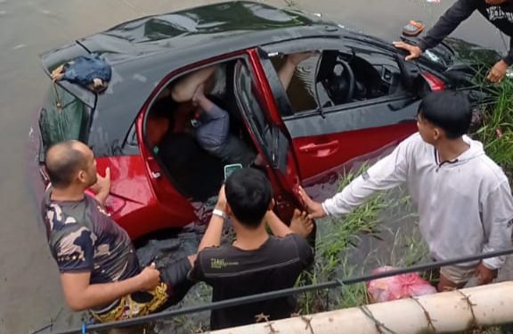 Mobil minibus yang mengalami kecelakaan dan tenggelam total di sungai tepi jalan.