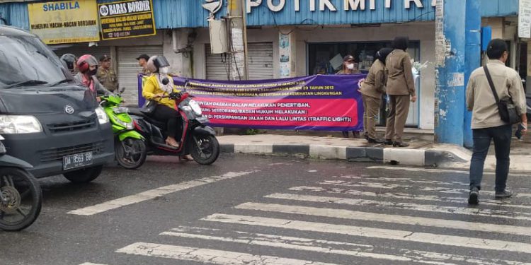 Petugas Satpol PP Banjaramsin bentangkan spanduk larangan memberi uang pengemis dan pengamen di jalanan saat sosialisasi Perda Penanganan Gepeng dan Anjal di Simpang Empat Jalan Belitung. (foto : shn/seputaran)