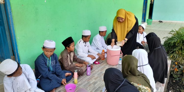 Seorang guru SDN Kelayan 1 Banjarmasin saat membagikan bubur Asyura kepada murid. (foto : shn/seputaran)