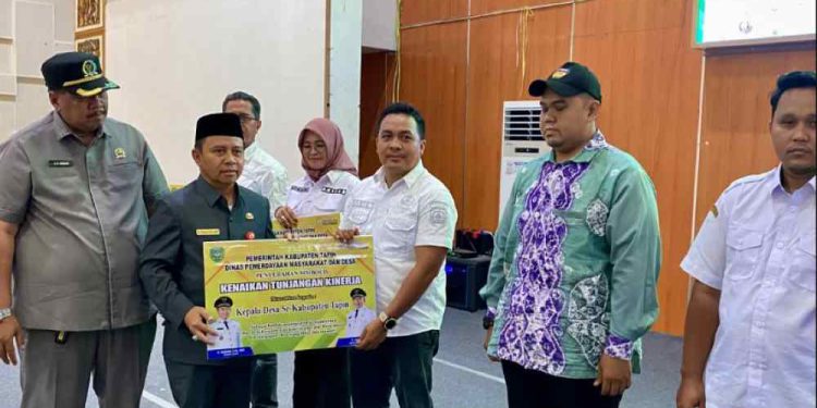 Bupati Tapin H Yamani secara simbolis menyerahkan kenaikan tunjangan kepada salah satu perangkat desa. (foto : istimewa)