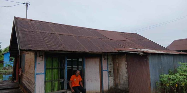 Muhammad Satar yang duduk di depan rumahnya yang kerap terendam. (foto : shn/seputaran)