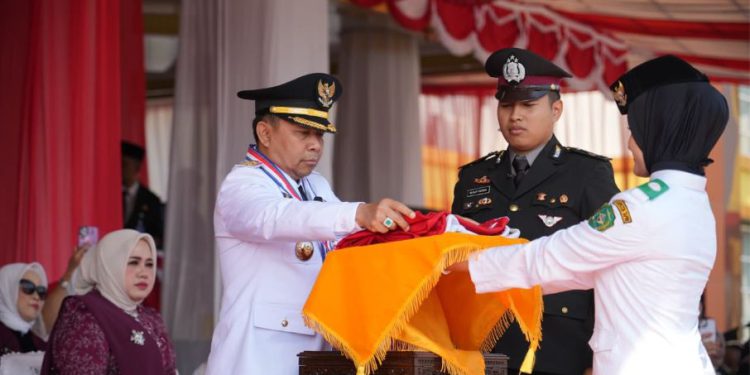 Bupati Tapin H Yamani saat menyerahkan bendera Merah Putih kepada Paskibraka untuk dikabarkan pada upacara peringatan HUT Kemerdekaan RI di Tapin. (foto : istimewa)